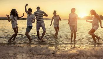 Gruppe junger Leute tanzt entspannt bei Sonnenuntergang am Meer
